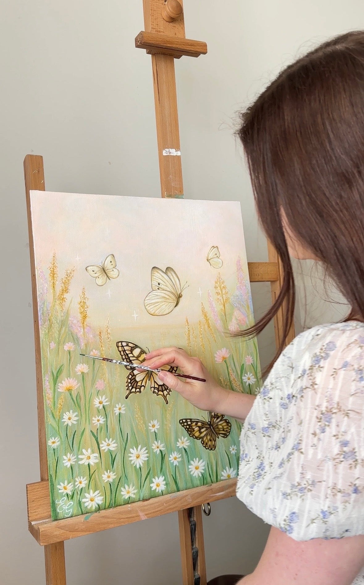 Female artist painting a butterfly scene on a canvas with an easel.