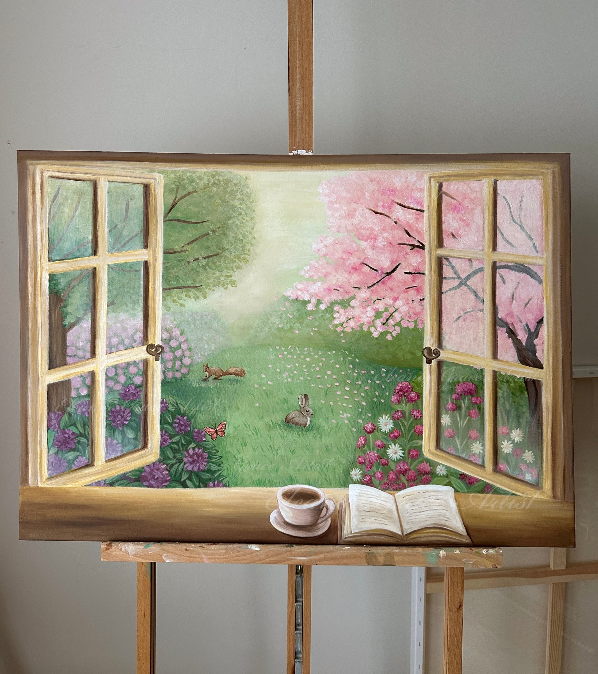 Painting of a garden scene through a window with a cup and book on an easel.